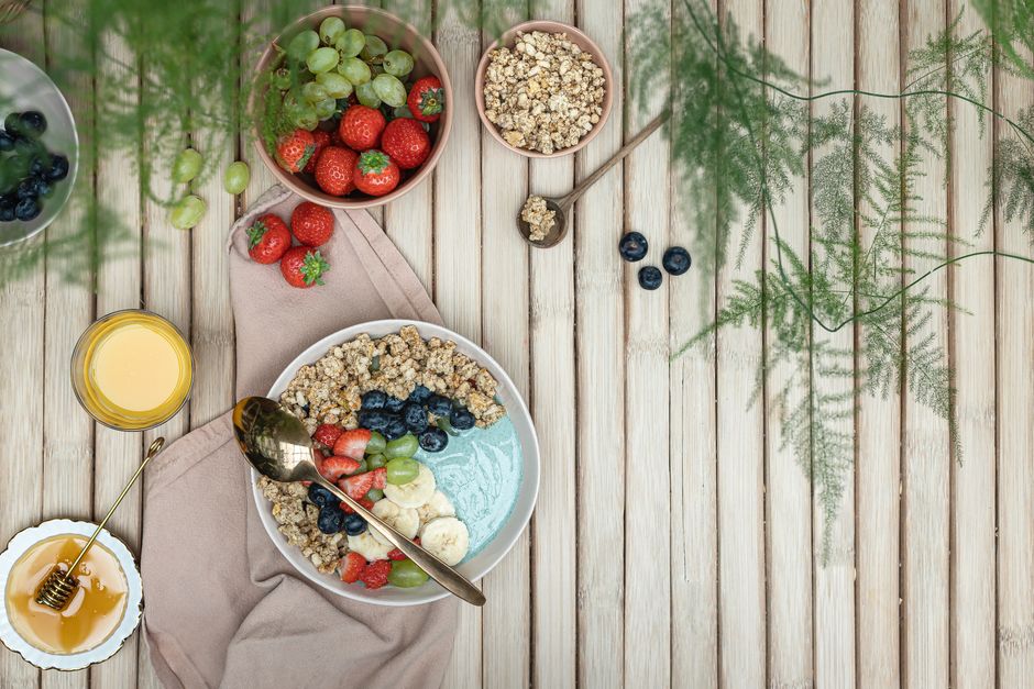 A colorful breakfast bowl with fresh fruits, granola, and honey on a rustic wooden table.